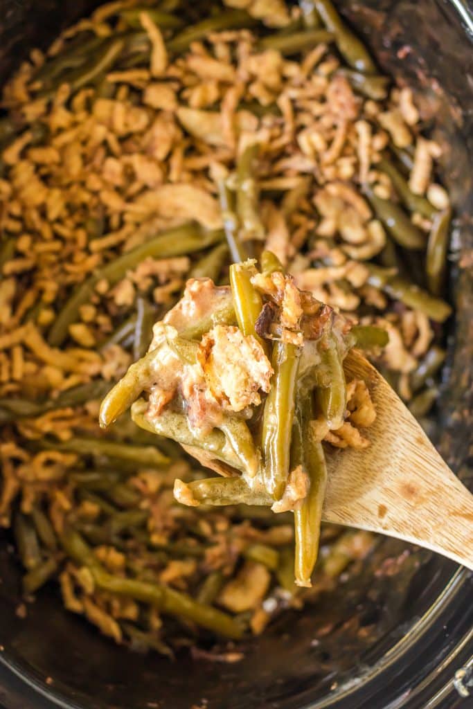 spoon lifting green bean casserole from a slow cooker.