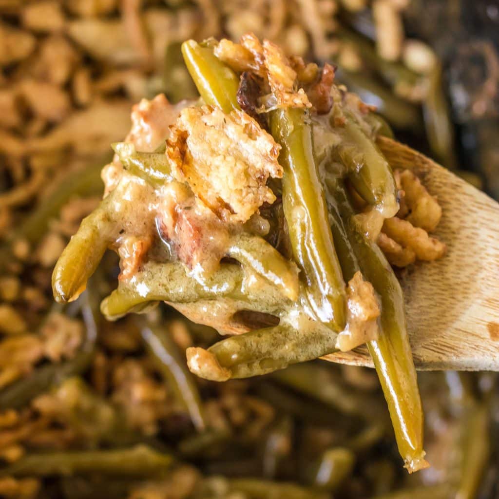 wooden spoon scooping green bean casserole from a slow cooker.