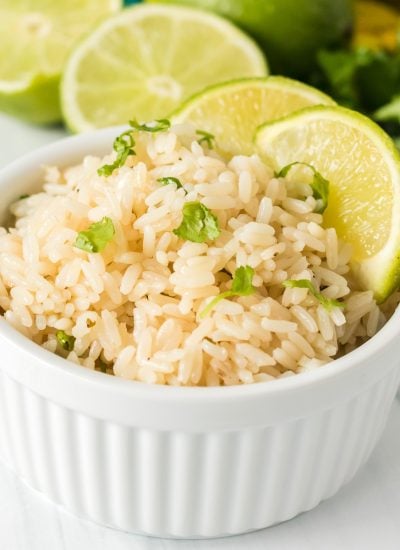 white bowl filled with rice topped with cilantro and lime wedges.