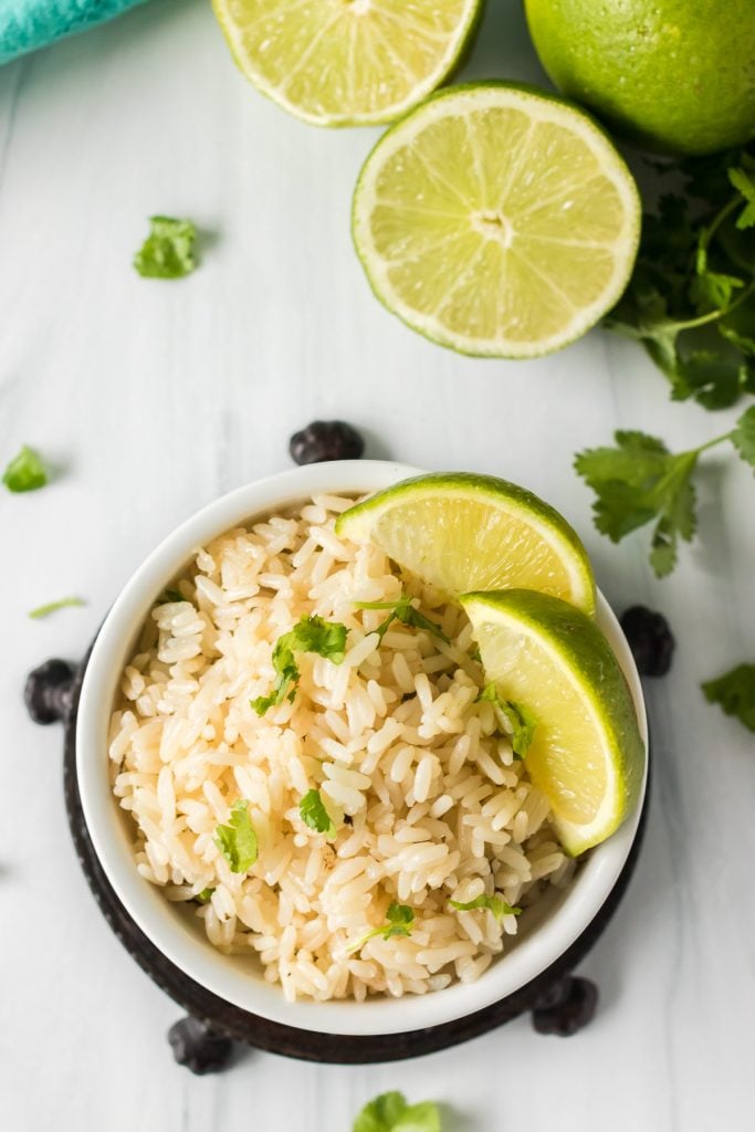 overhead shot of rice in a bowl topped with lime wedges & cilantro.