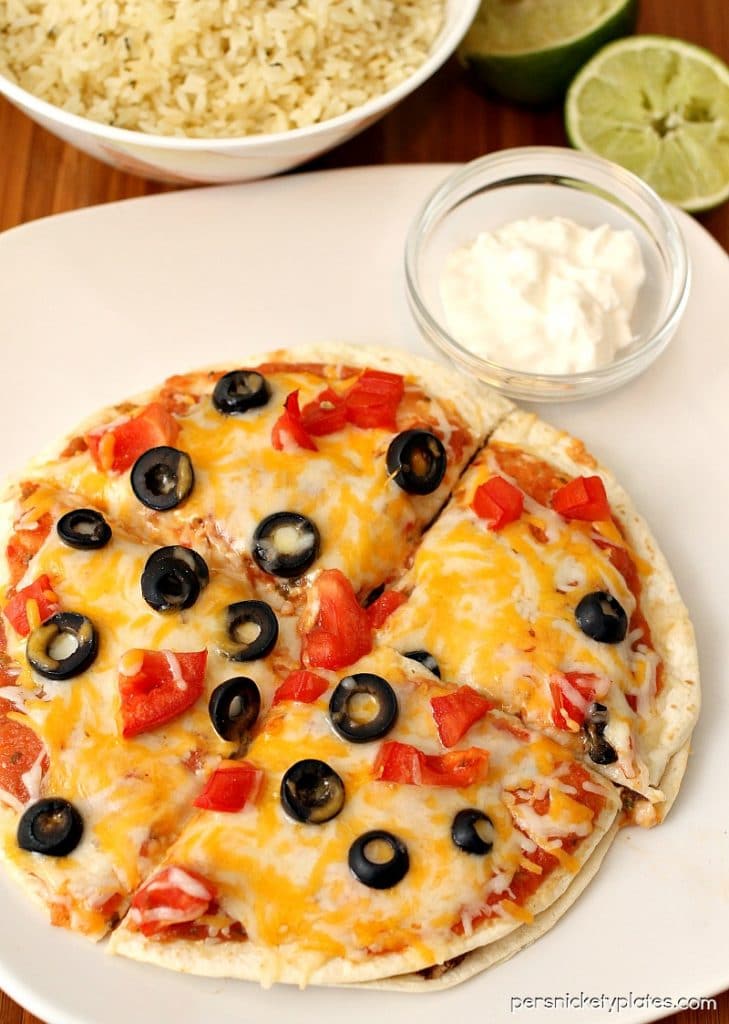 mexican pizza with a side of sour cream on a white plate