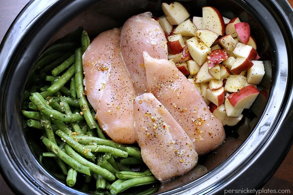 overhead shot of raw chicken in a crockpot with green beans and potatoes.