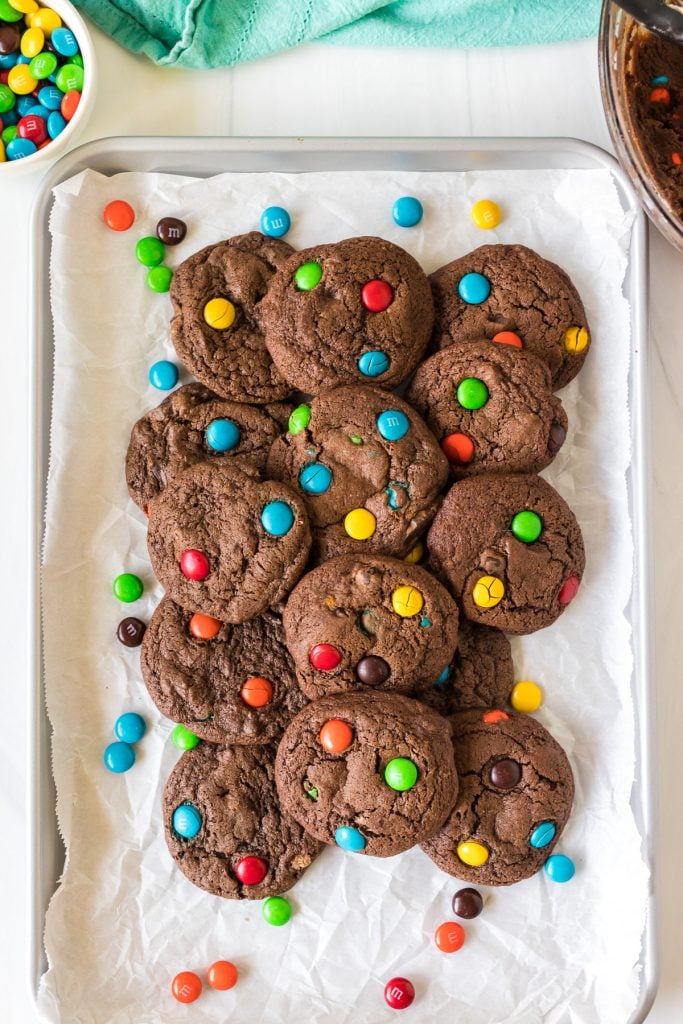overhead shot of pile of colorful M&M brownie cookies on a baking sheet.