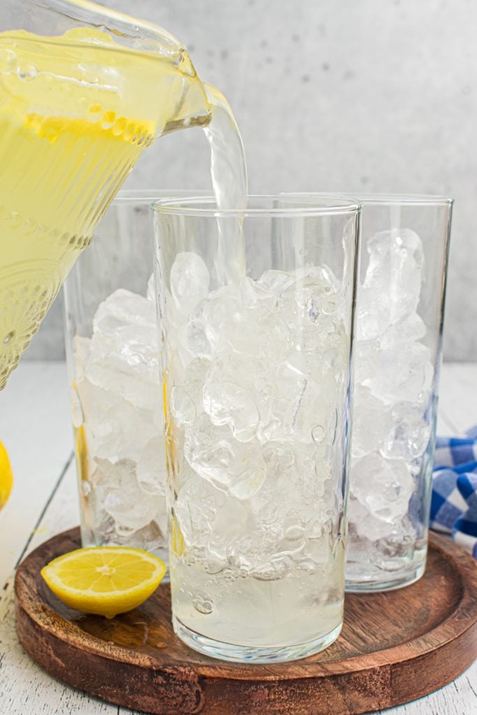 lemonade being poured into glass cups full of ice.