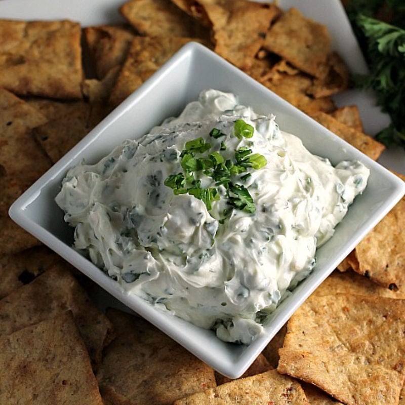 garlic herb dip in square bowl surrounded by chips