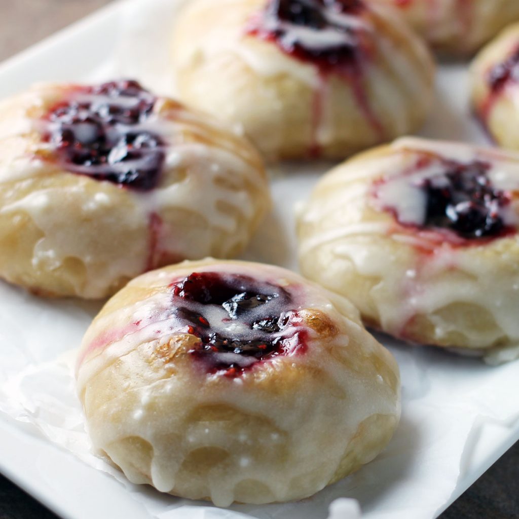 raspberry thumbprint donuts on a white plate with glaze