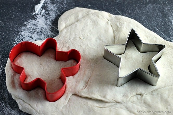 a gingerbread man and star shaped cookie cutters pressing into bread dough
