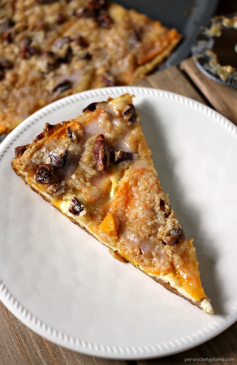 Peach Crumble Fruit Pizza is made on a cake batter crust, piled with thinly sliced fresh peaches and topped with a crumble and pecans and drizzled with a cinnamon sugar glaze. | www.persnicketyplates.com