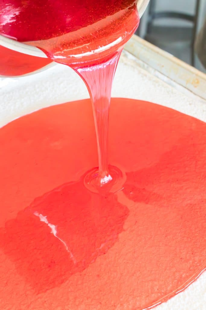 red sugar mixture pouring onto a baking sheet.
