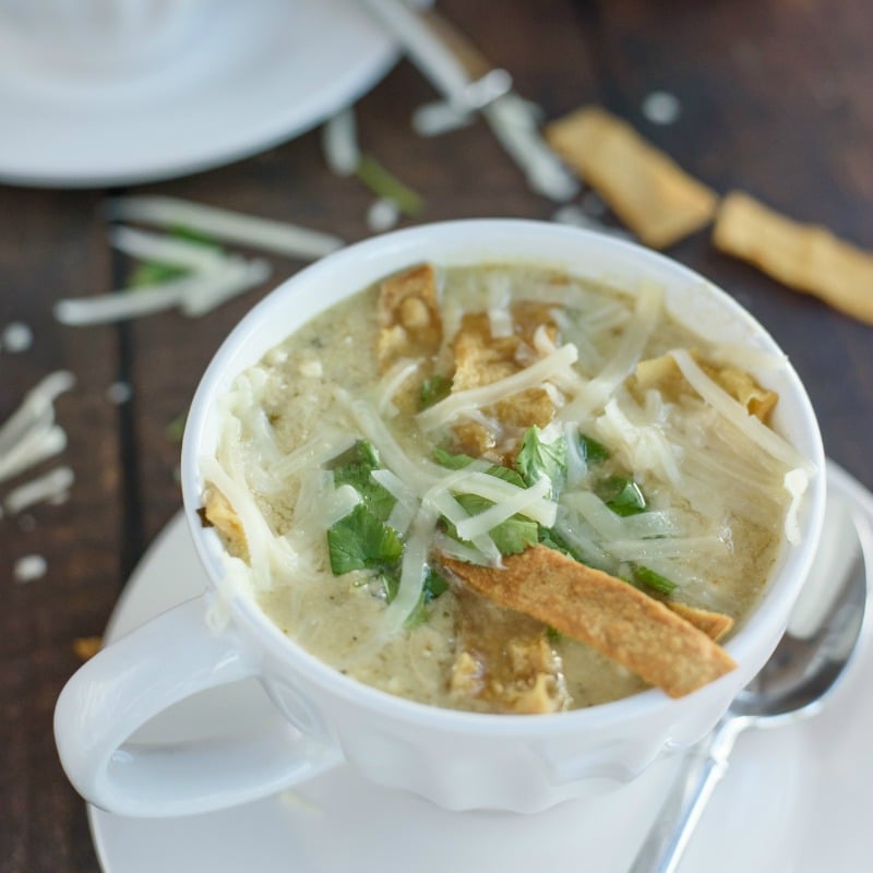 white bowl of slow cooker green chile chicken enchilada soup topped with cheese & tortilla strips