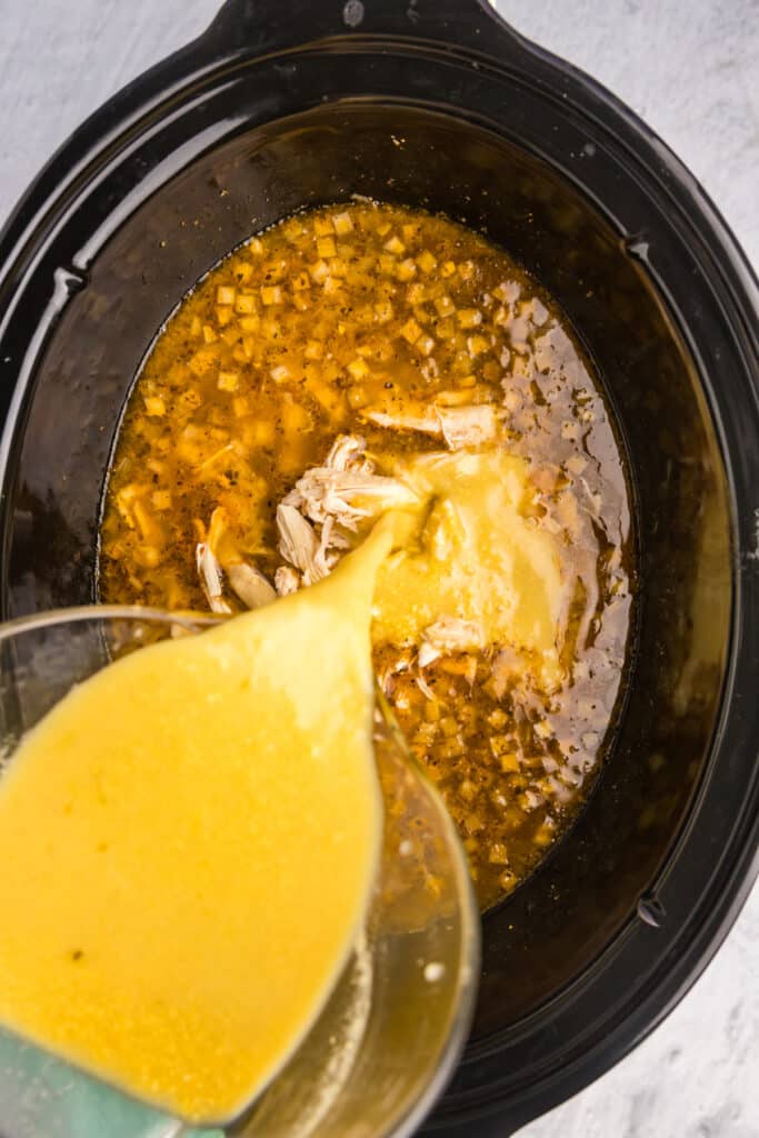 sauce pouring into a crockpot of soup.