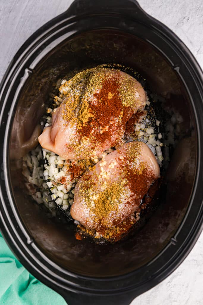 overhead shot of chicken breasts and seasonings in a crockpot.