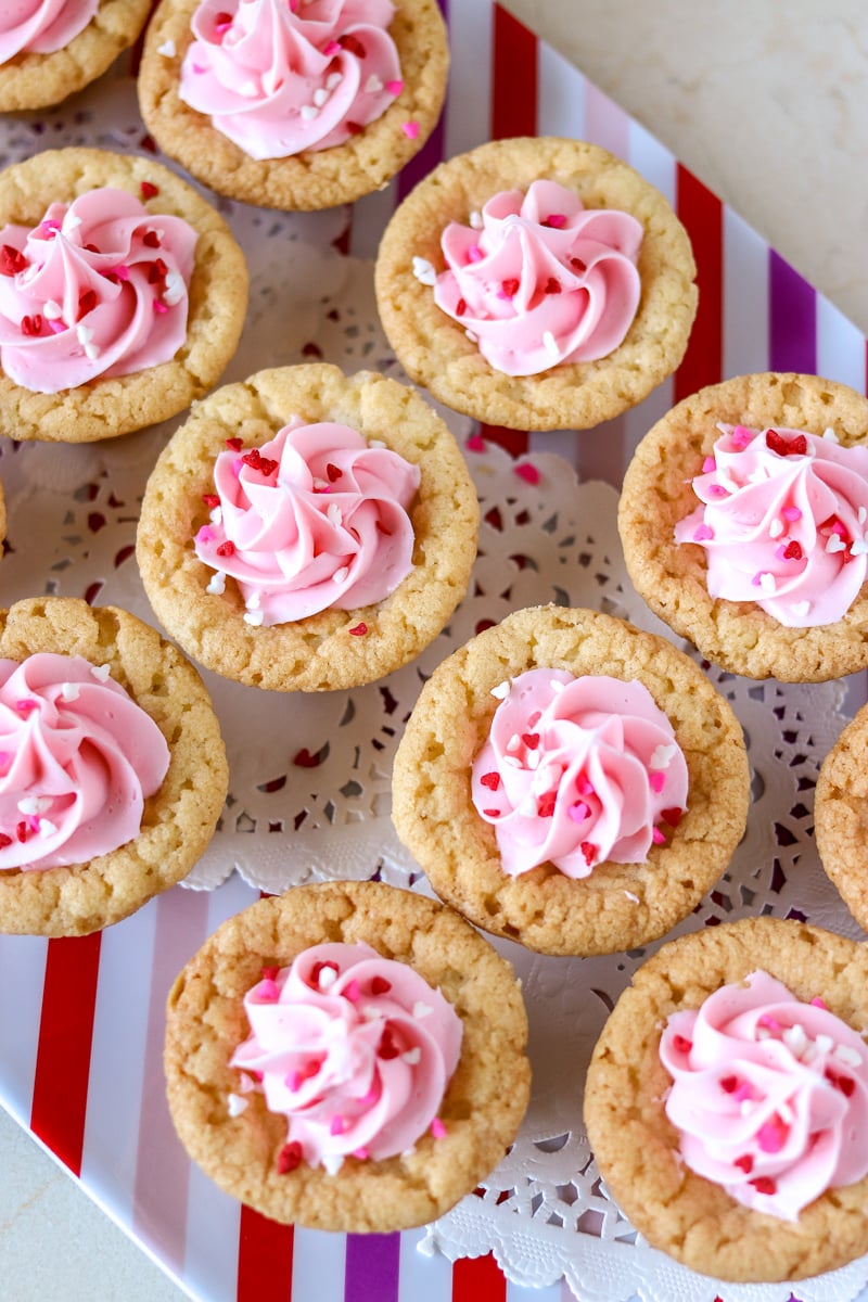 Valentine Sugar Cookie Cups are a simple, semi-homemade treat that you can whip up in no time! A sugar cookie base filled with pink frosting and topped with Valentine sprinkles. | www.persnicketyplates.com