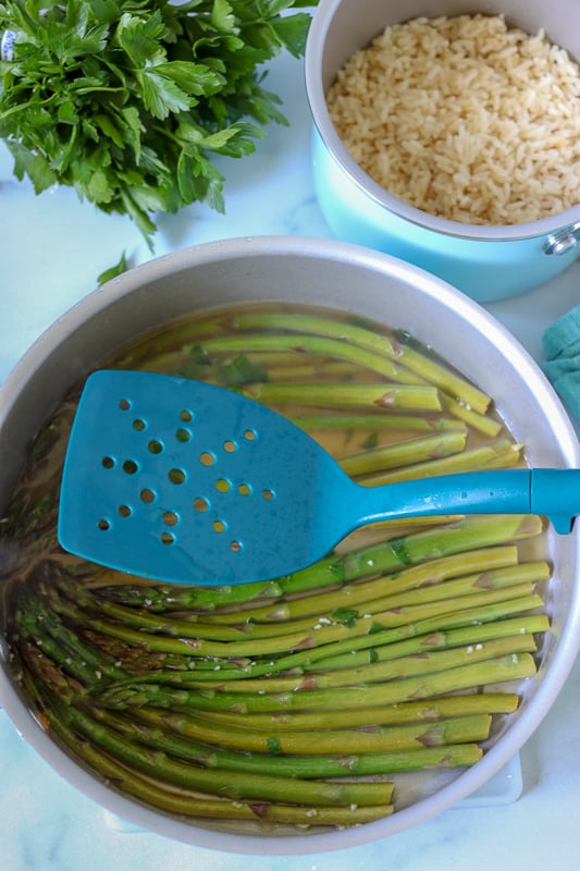 overhead shot of pan of asparagus and pot of rice with spatula