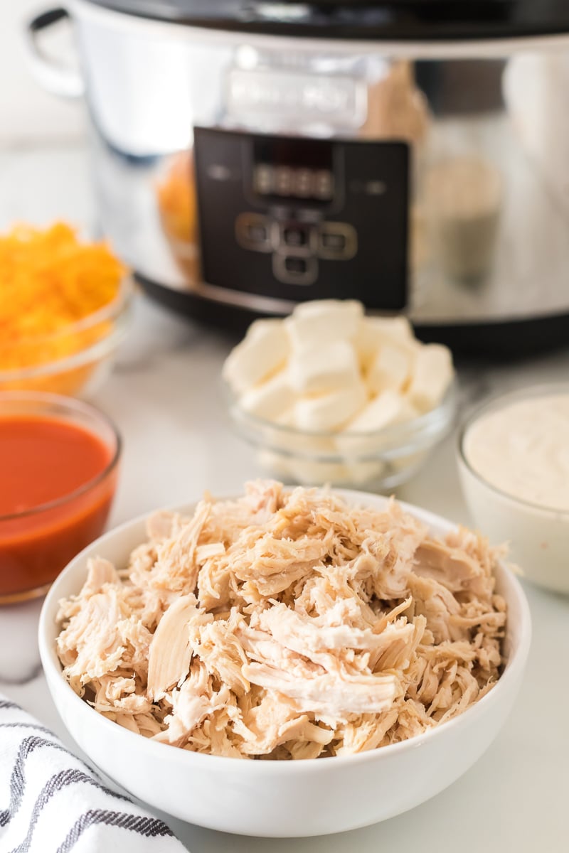 bowl of shredded chicken with slow cooker in background