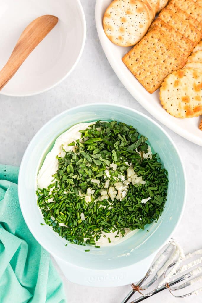 overhead shot of cream cheese and herbs in a mixing bowl.
