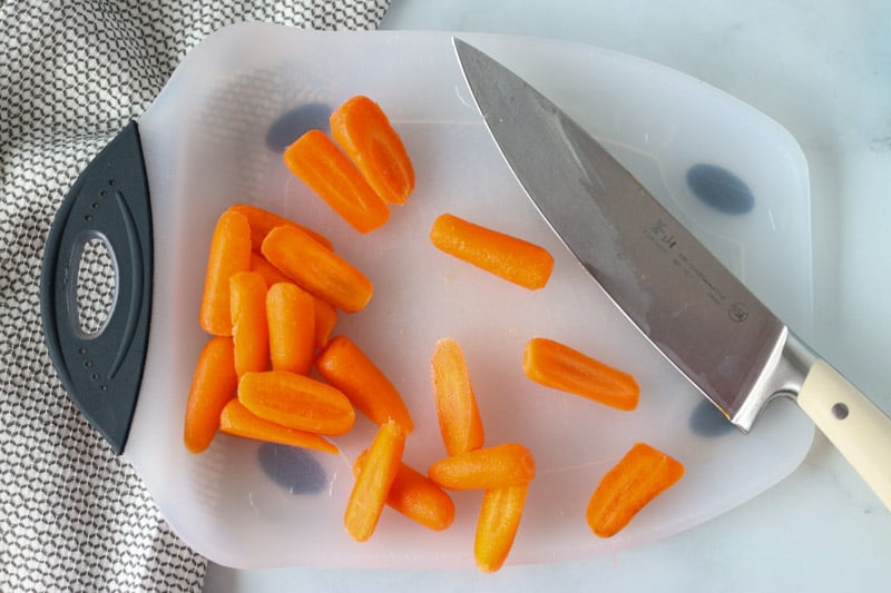 baby carrots on a cutting board with a knife
