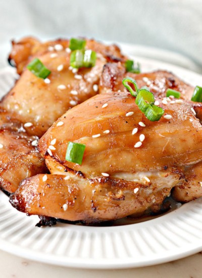 air fried sticky chicken thighs on a white plate with green onion & sesame seed garnish