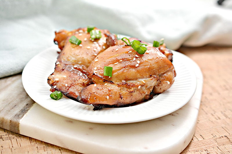 air fried sticky chicken thighs on a white plate with green onion & sesame seed garnish