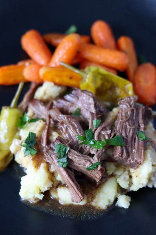 plate of mississippi pot roast served over mashed potatoes with roasted carrots