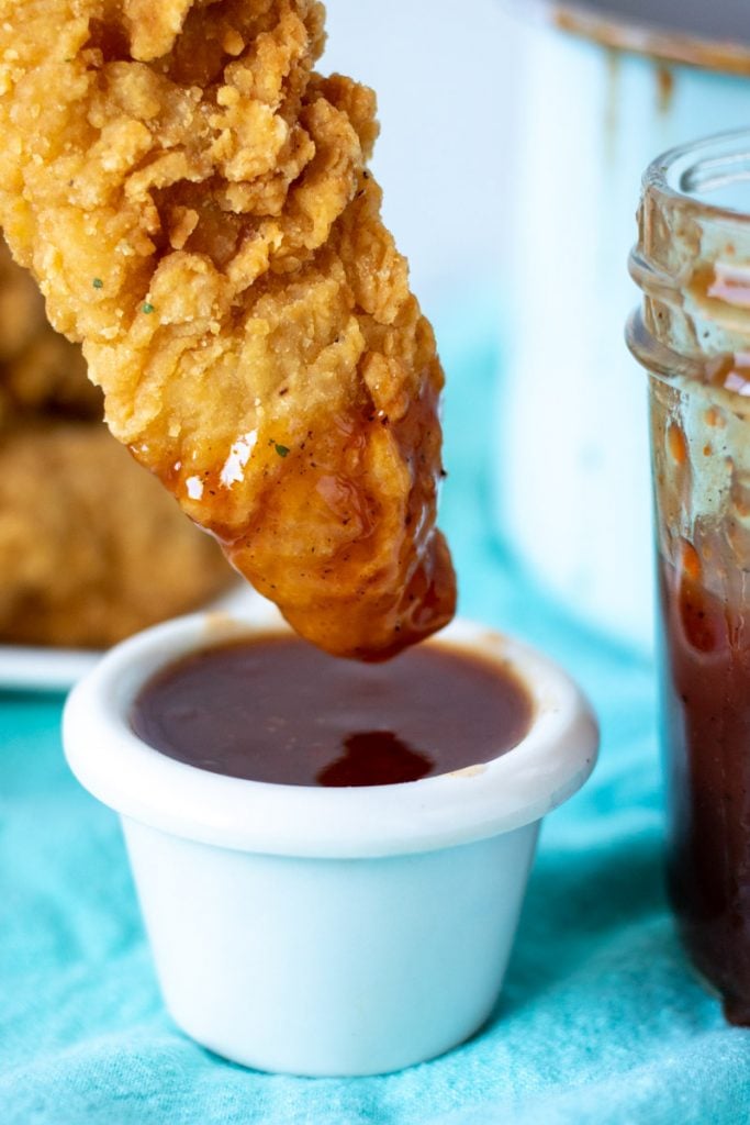 chicken tender being dipped into bbq sauce