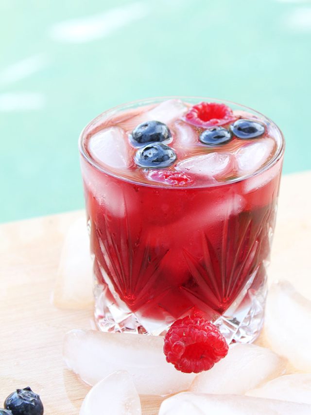 glass of berry sangria surrounded by ice cubes & fresh fruit