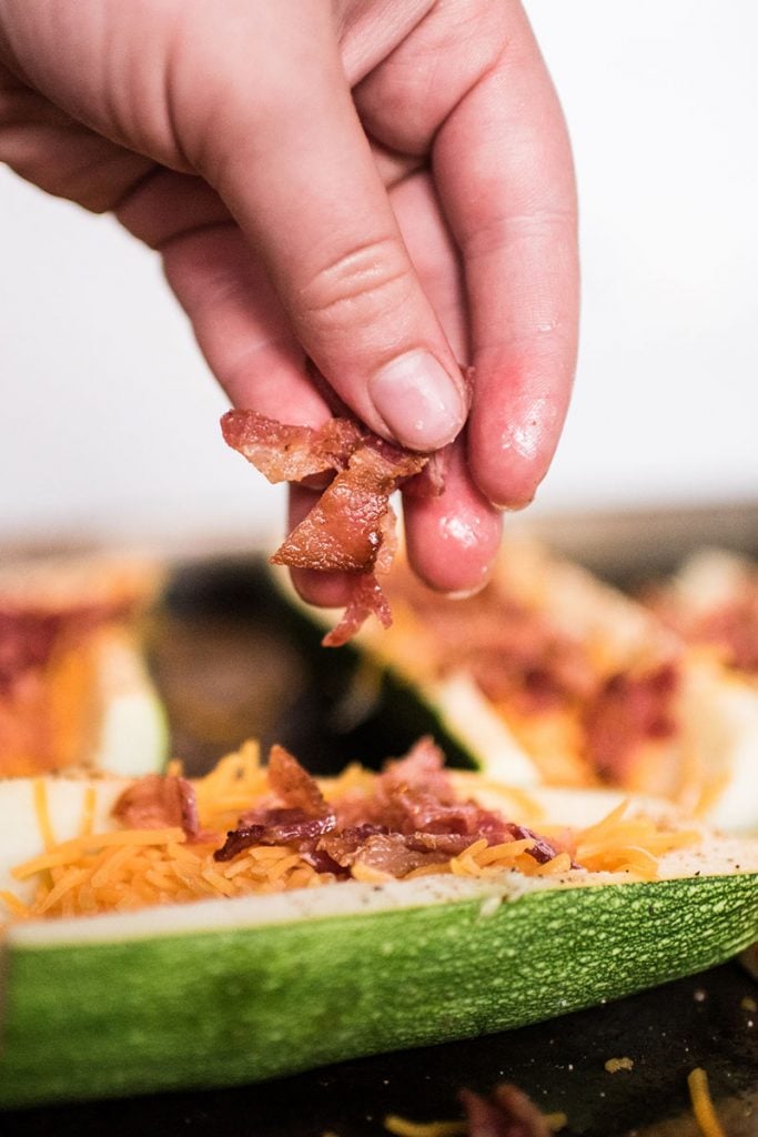 hand sprinkling bacon on zucchini skins