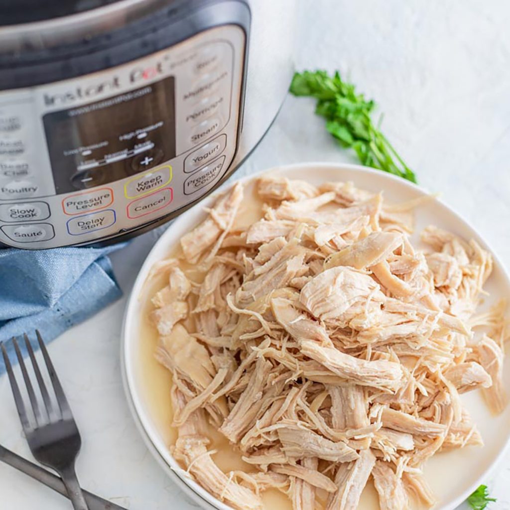 plate of shredded chicken breasts next to an instant pot