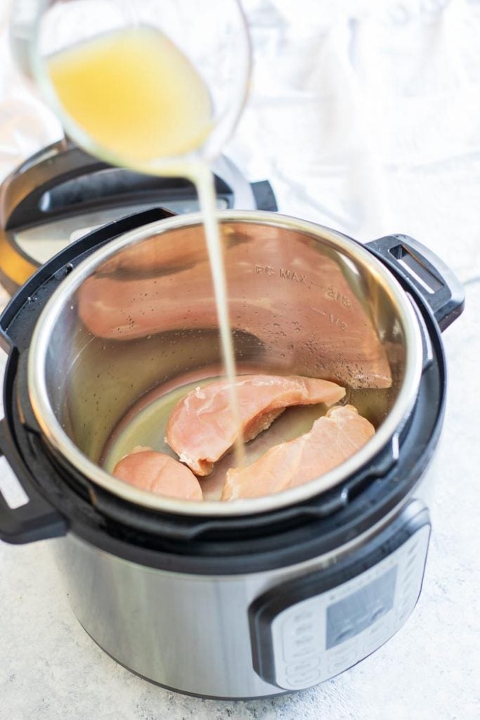 pouring chicken broth into instant pot with chicken breasts
