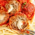 melty mozzarella in the center of a meatball on a bed of noodles.