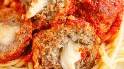melty mozzarella in the center of a meatball on a bed of noodles.