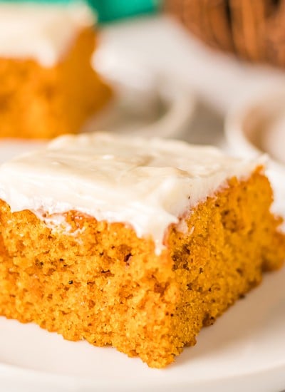 close up shot of a pumpkin bar topped with cream cheese frosting on a white plate