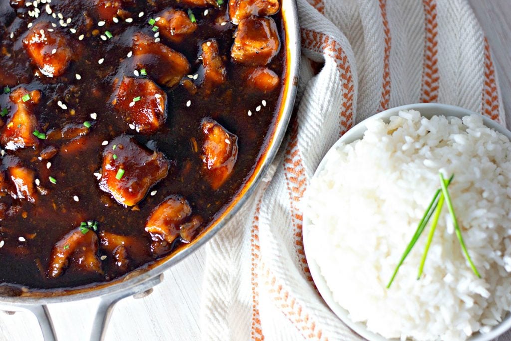 bourbon chicken in a skillet next to a bowl of white rice