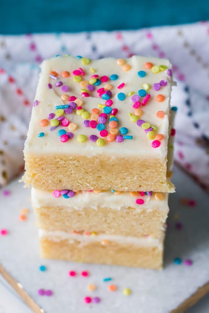 stack of 3 sugar cookie bars topped with frosting and rainbow sprinkles.