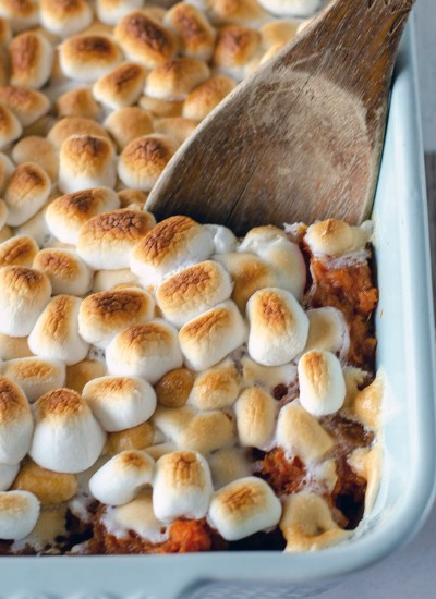wooden spoon dipping into sweet potato casserole topped with marshmallows