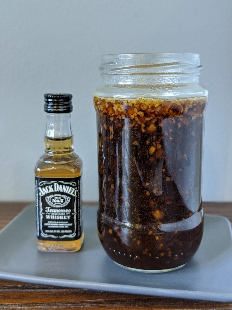 jar of jack daniels sauce sitting next to a shooter of jack daniels whiskey.
