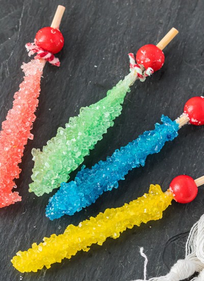 four sticks of rock candy in pink, green, blue, and yellow on a grey slab