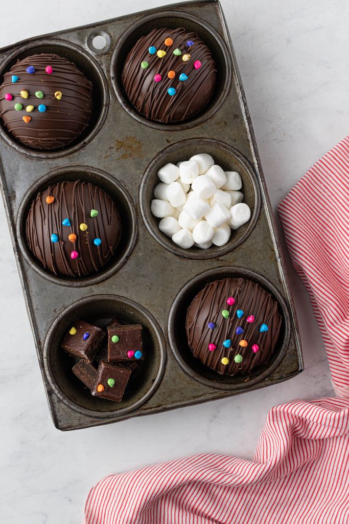 cupcake tray filled with hot chocolate bombs, mini marshmallows, and cosmic brownie bites