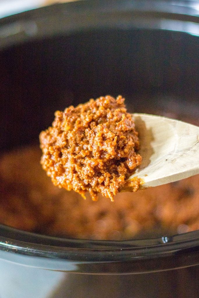 wooden spoon scooping hot dog chili from crockpot