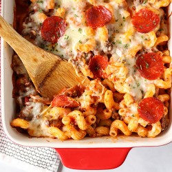 wooden spoon scooping pizza pasta bake from a baking dish