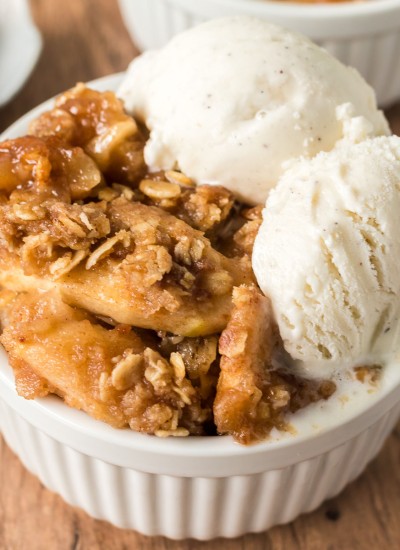 apple crisp topped with vanilla ice cream in a white bowl