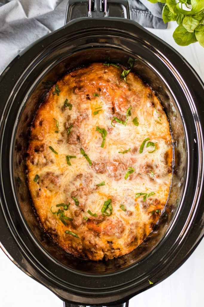 overhead shot of lasagna in slow cooker topped with chopped basil