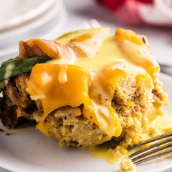portion of eggs benedict casserole, drizzled with hollandaise, on a white plate with a fork
