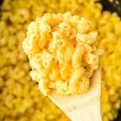 wooden spoon scooping mac and cheese from a slow cooker