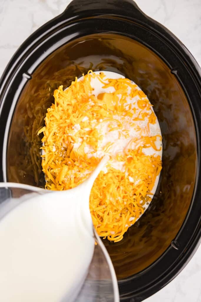 milk pouring into a slow cooker with cheese & noodles.