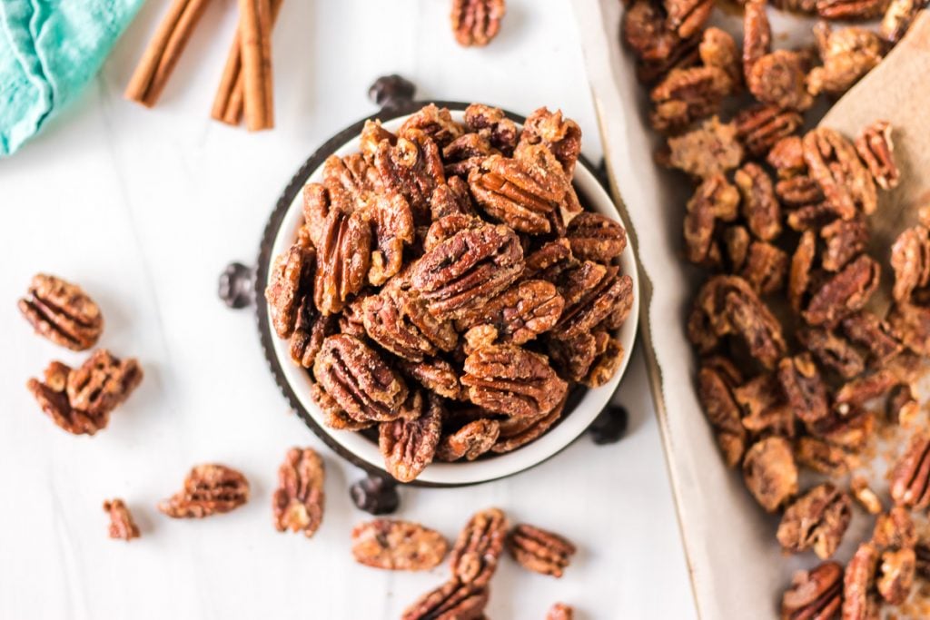 bowl of candied pecans next to a baking sheet