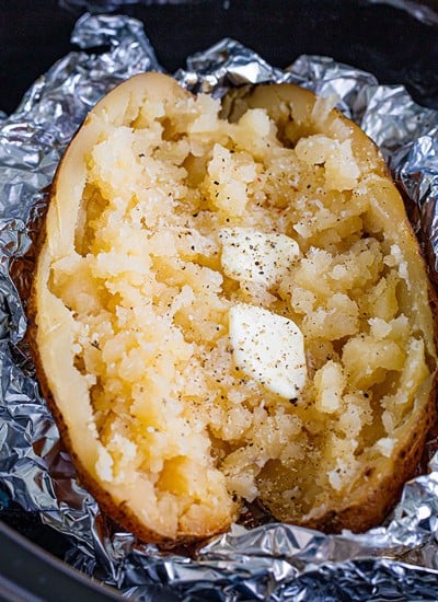 baked potato in foil split open with butter sitting in a slow cooker