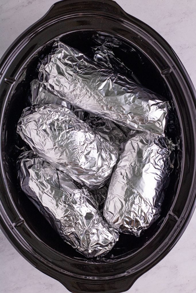 overhead shot of foil wrapped potatoes in a slow cooker