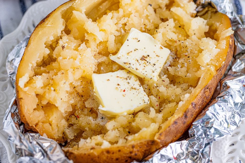 closeup of baked potato split open with butter, salt, and pepper