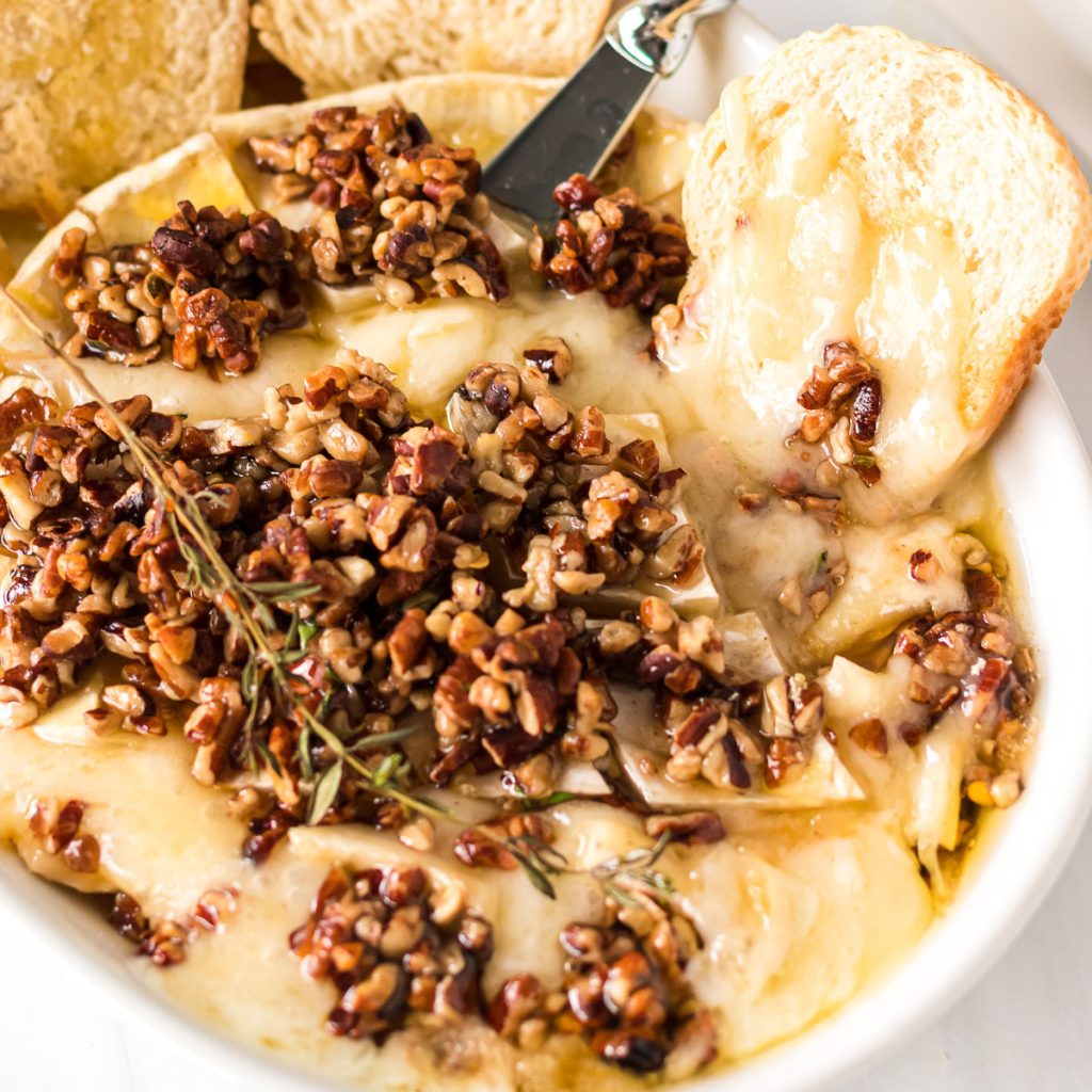 bread and a cheese knife stuck into melty baked brie with pecans and honey